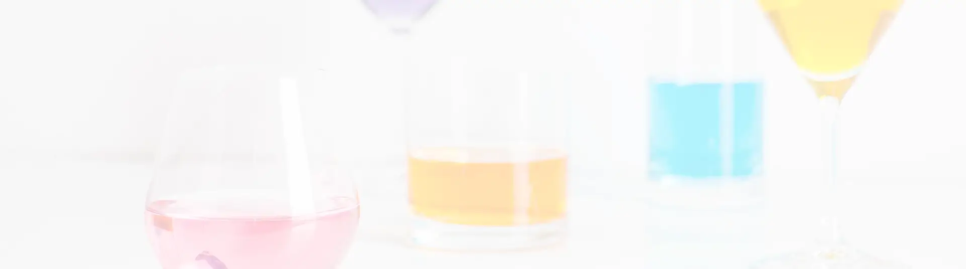 Cristina Lain Una variedad de cócteles coloridos en vasos, incluidos tragos rosados, amarillos, azules y anaranjados, dispuestos sobre una superficie de color claro. Las bebidas están en copas de cóctel o de vino, ligeramente desenfocadas, creando una presentación suave y vibrante. Branding Fotografía Mentorias