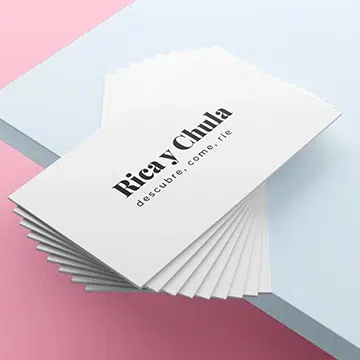 Cristina Lain Una pila de tarjetas de presentación blancas sobre una superficie celeste y rosa. La tarjeta superior dice "Rica Y Chula" con el eslogan "descubre, come, ríe" en letras negras. Branding Fotografía Mentorias
