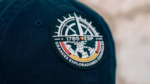 Cristina Lain Primer plano de una gorra azul marino que muestra la marca Expert con un parche circular con un diseño de brújula. El texto "1785 ESP" y "GRANDES EXPLORADORES ESPAÑOLES" rodean elegantemente el emblema, capturando el espíritu de aventura y exploración. Branding Fotografía Mentorias