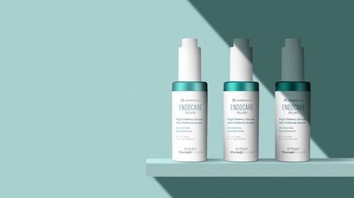 Cristina Lain Tres frascos de productos para el cuidado de la piel en blanco y verde azulado con la etiqueta "Endocare" están ordenados cuidadosamente en un estante azul claro. El fondo, que refleja la serena marca, es de un azul claro a juego y la escena está muy iluminada con sombras suaves. Branding Fotografía Mentorias
