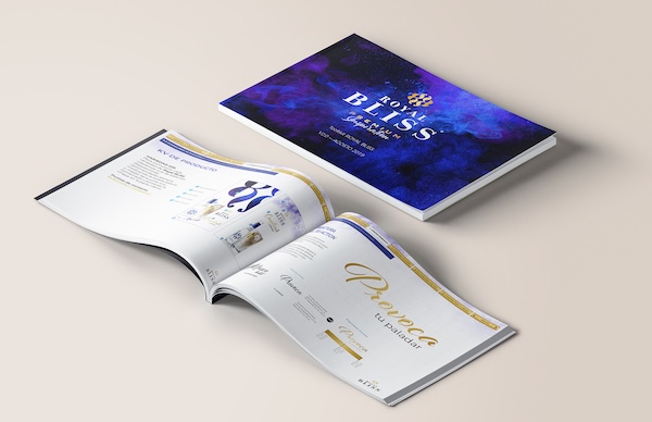 Cristina Lain Un catálogo titulado "Royal Bliss Lifestyle" con una impresionante cubierta azul y violeta se abre sobre una superficie beige. Las páginas abiertas muestran diseños elegantes, gráficos de marca y texto en armoniosos tonos azules y dorados. Branding Fotografía Mentorias