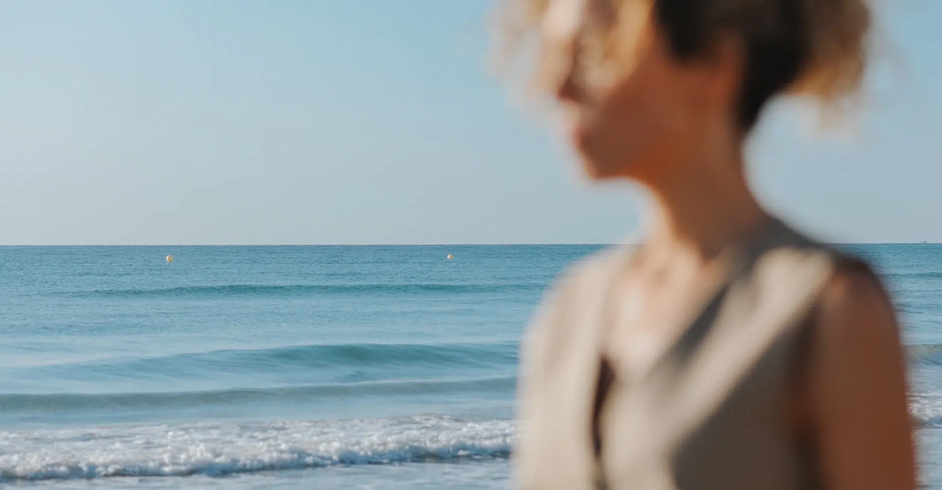 Cristina Lain Imagen borrosa de una persona parada junto al mar. El foco está en las tranquilas olas azules del océano y el cielo despejado al fondo. Branding Fotografía Mentorias