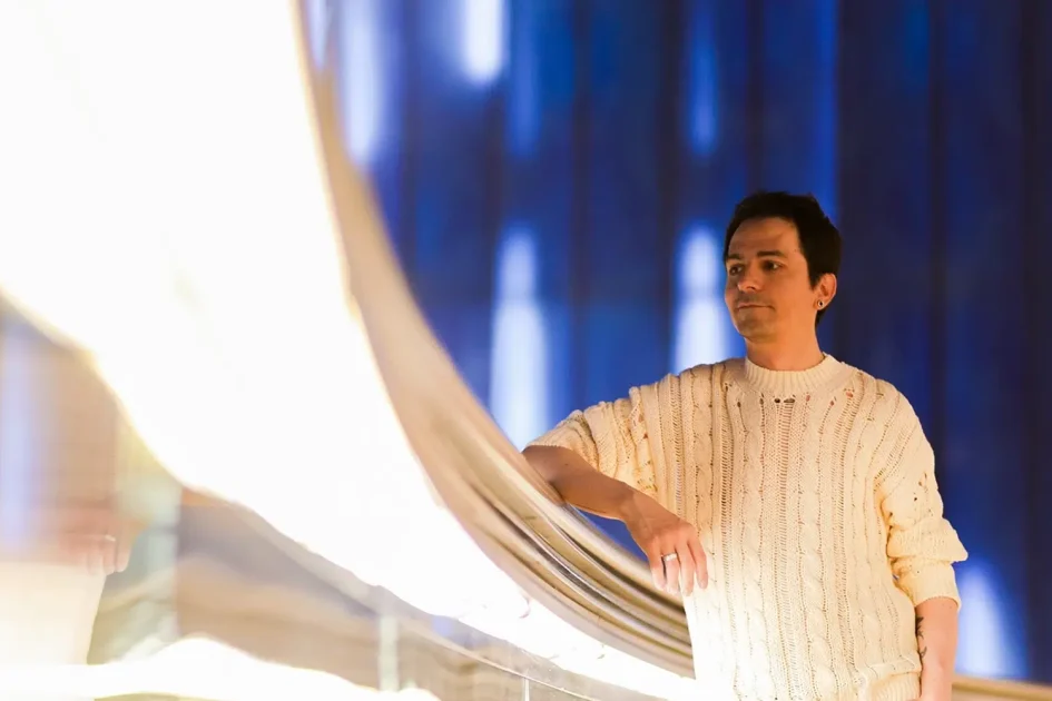Cristina Lain Una persona con un suéter color crema se encuentra pensativa junto a una barandilla reflectante. El fondo presenta un efecto borroso con luces brillantes y un fondo azul profundo, lo que crea una atmósfera artística e introspectiva. Branding Fotografía Mentorias