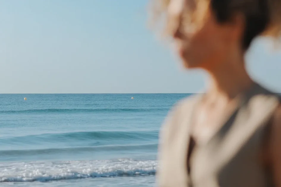 Cristina Lain Imagen borrosa de una persona parada junto al mar. El foco está en las tranquilas olas azules del océano y el cielo despejado al fondo. Branding Fotografía Mentorias